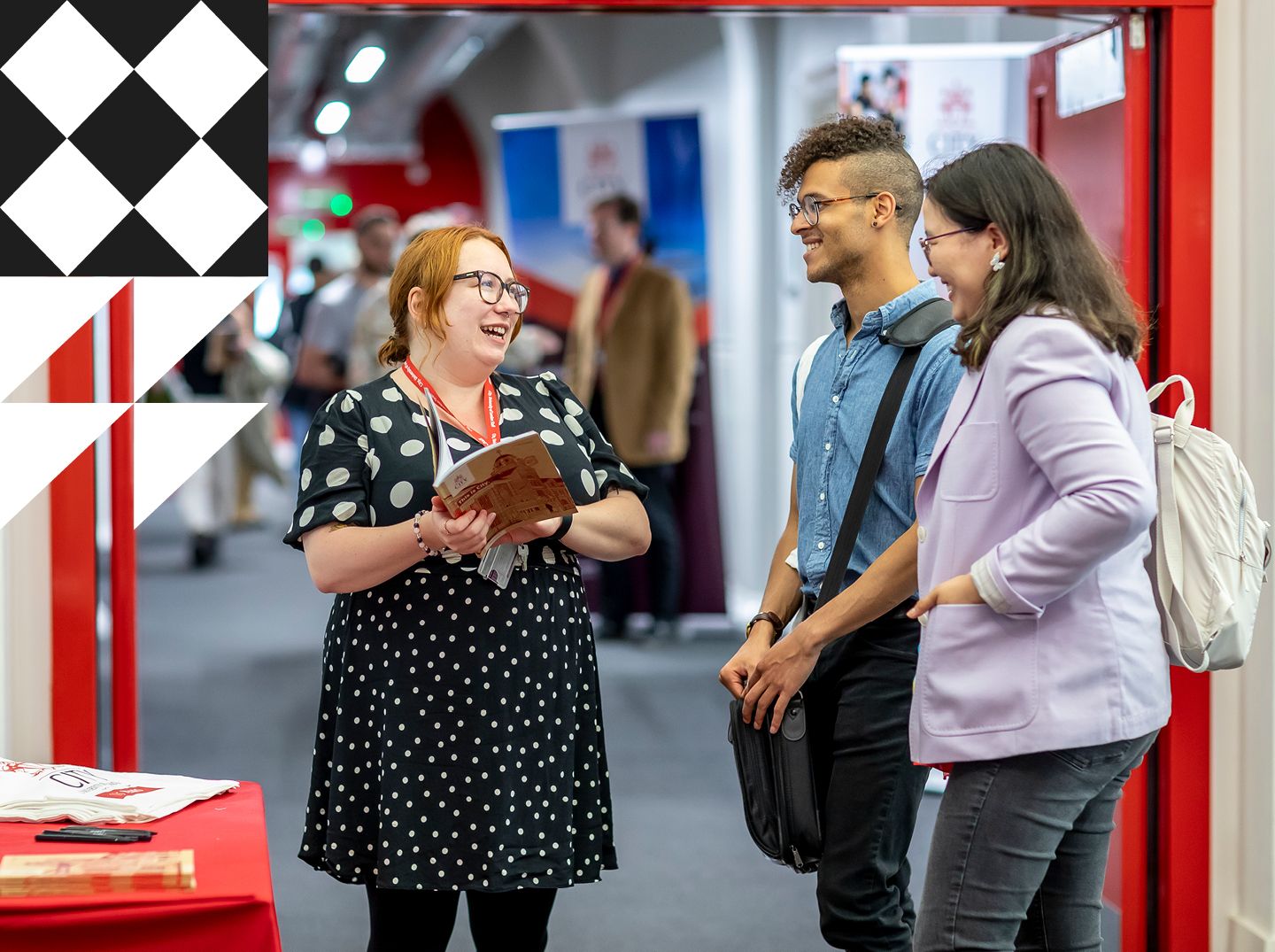 Inside campus corridor, a City staff member is holding a prospectus helping two prospective postgraduate students.