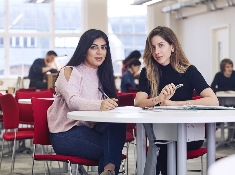 2 students sit at a desk and look into the camera