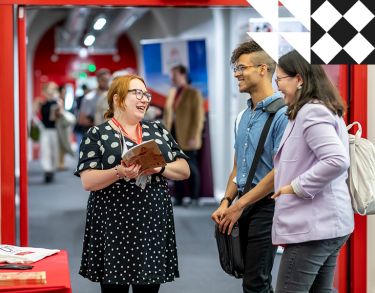 Inside campus corridor, a City staff member is holding a prospectus helping two prospective postgraduate students.