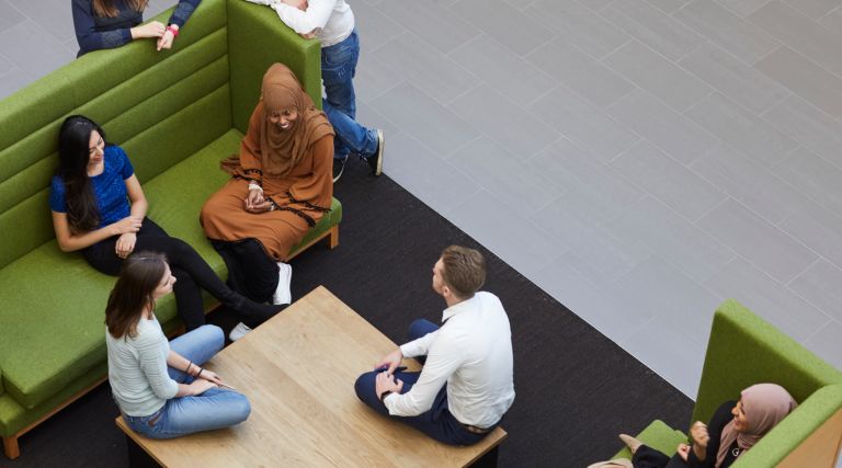 Group of students chatting while sitting on green sofa