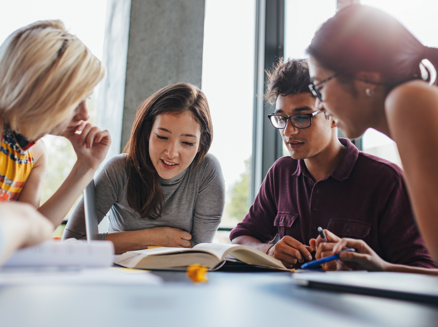 Four students around a table chatting and writing on paper. 