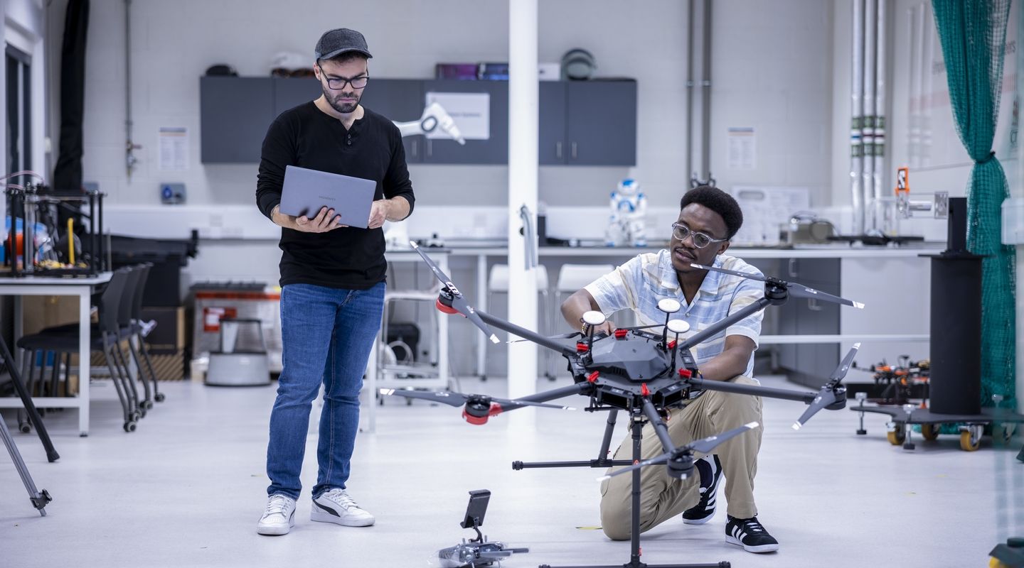 Two students, one with a laptop and the other working on a device