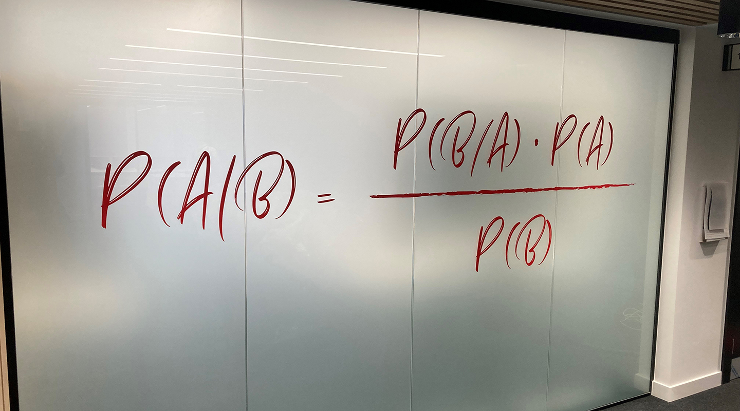Bayes theorem written large handwriting-style on a glass partition.