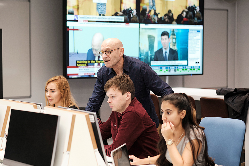 Three students using computers whilst male academic leans over chair to look at screen