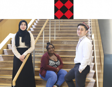 Three young students facing forward and smiling in front of City's indoor stairwell