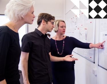 Three students looking at personas and wireframes on whiteboard