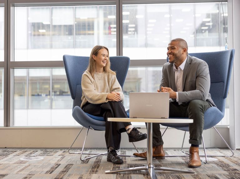 Male and female student in in conversation, sitting in chairs.