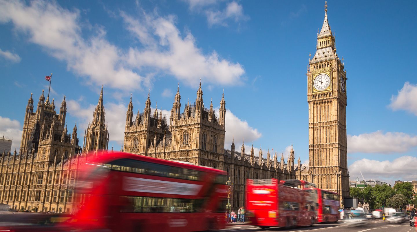Red London buses driving in front of Big Ben and the Houses of Parliament.