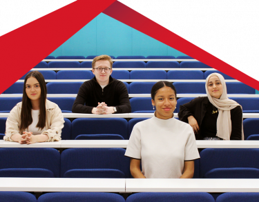 Four students face forward sitting together in lecture hall.