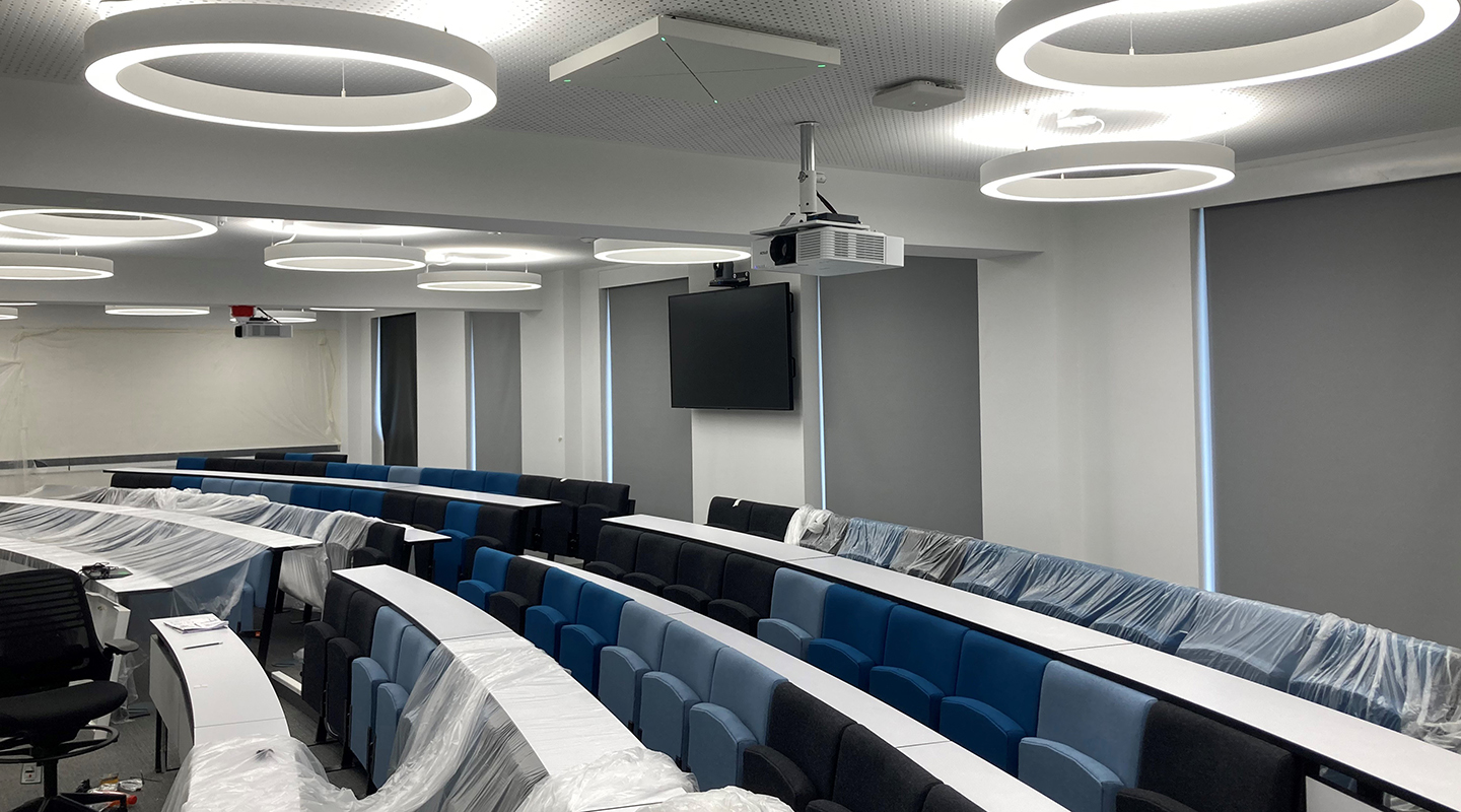 Curved lecture theatre with partially removed dustsheets. White ring shaped overhead lights are a design feature.