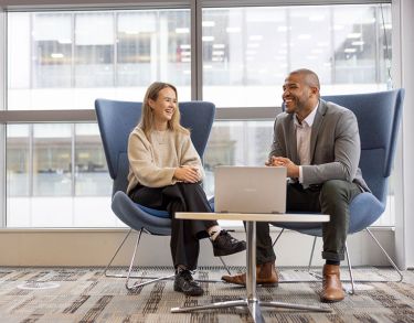 Male and female student in in conversation, sitting in chairs.