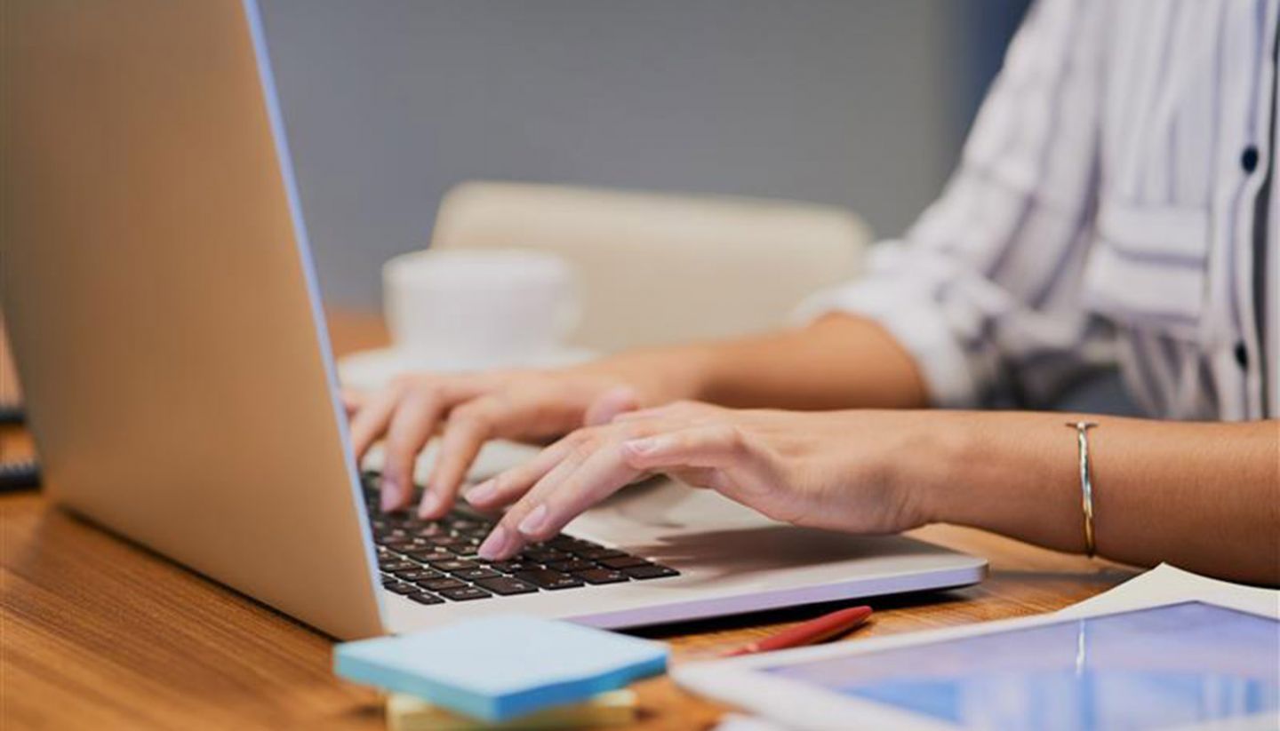 Hands typing at a laptop resting on a table
