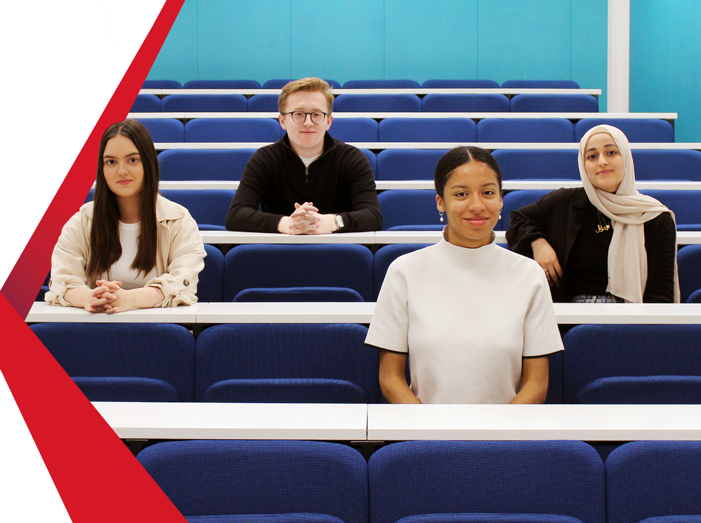 Four students face forward sitting together in lecture hall.