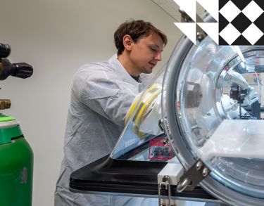 Male researcher wearing a white lab coat and gloves working on optic sensor monitoring system.