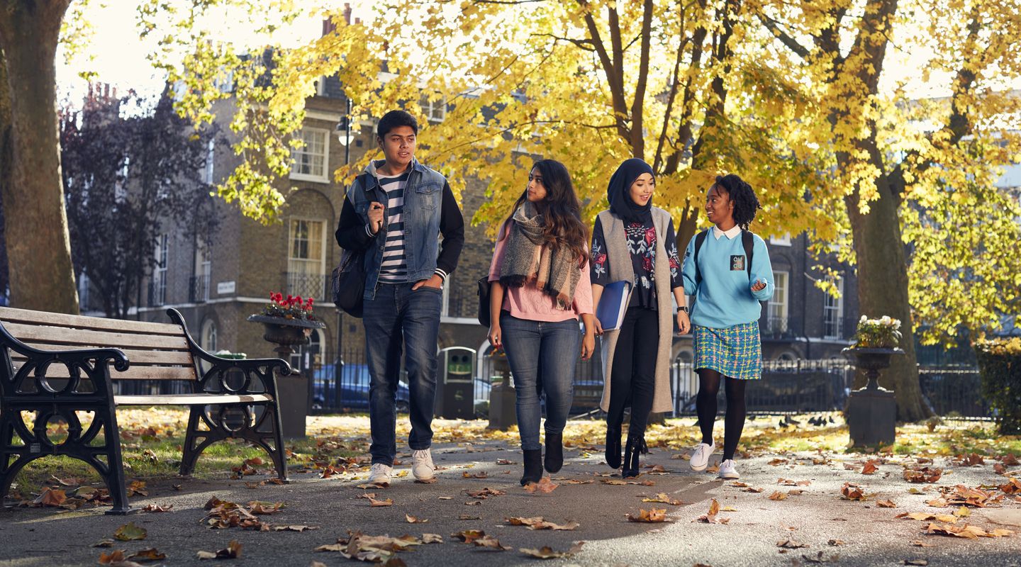 Four students walking outside through leaves on the ground