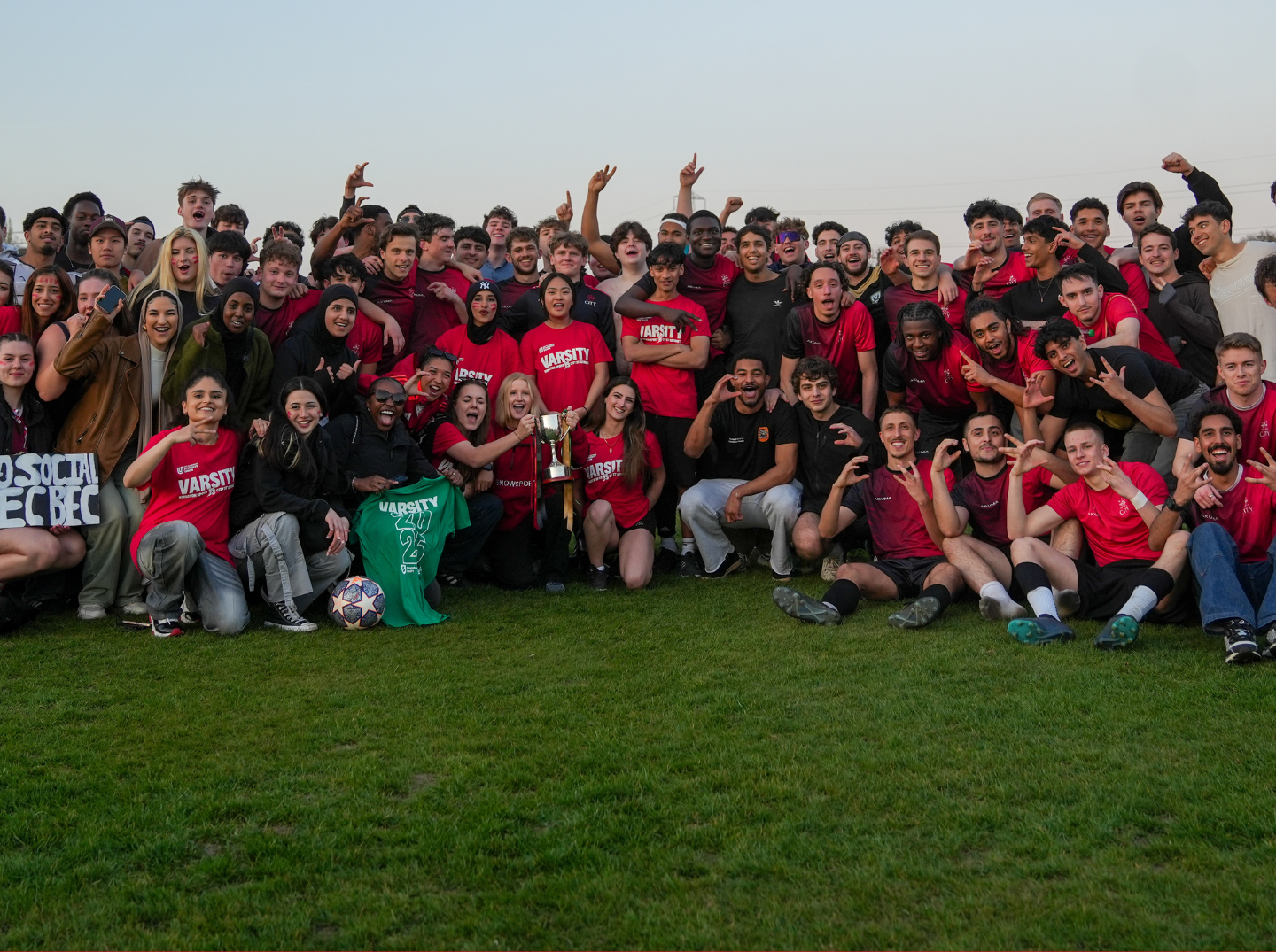 Group photo of City St George's sports teams in Kingston field celebrating Varsity win with trophy