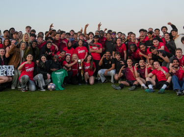 Group photo of City St George's sports teams in Kingston field celebrating Varsity win with trophy