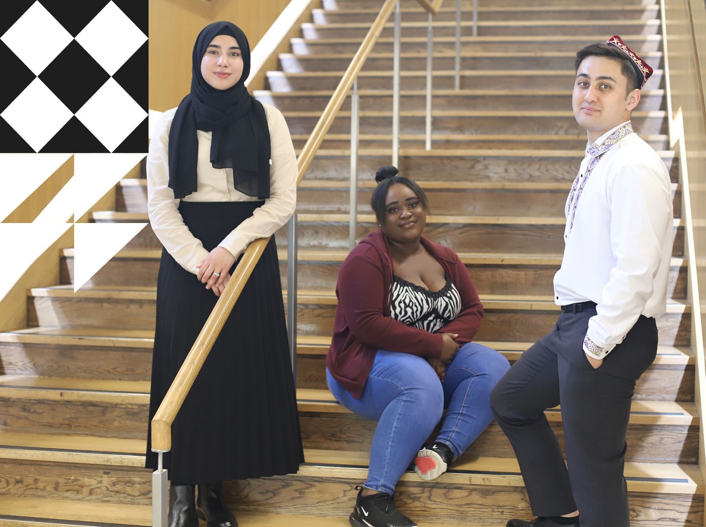 Three young students facing forward and smiling in front of City's indoor stairwell