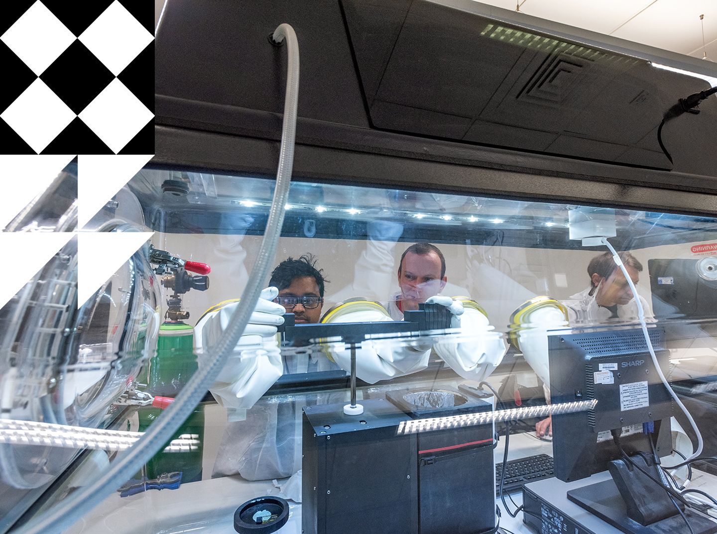 Three male researchers wearing white lab coats and gloves working on optic sensor monitoring system.