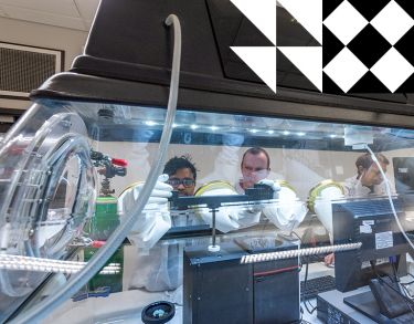 Three male researchers wearing white lab coats and gloves working on optic sensor monitoring system.