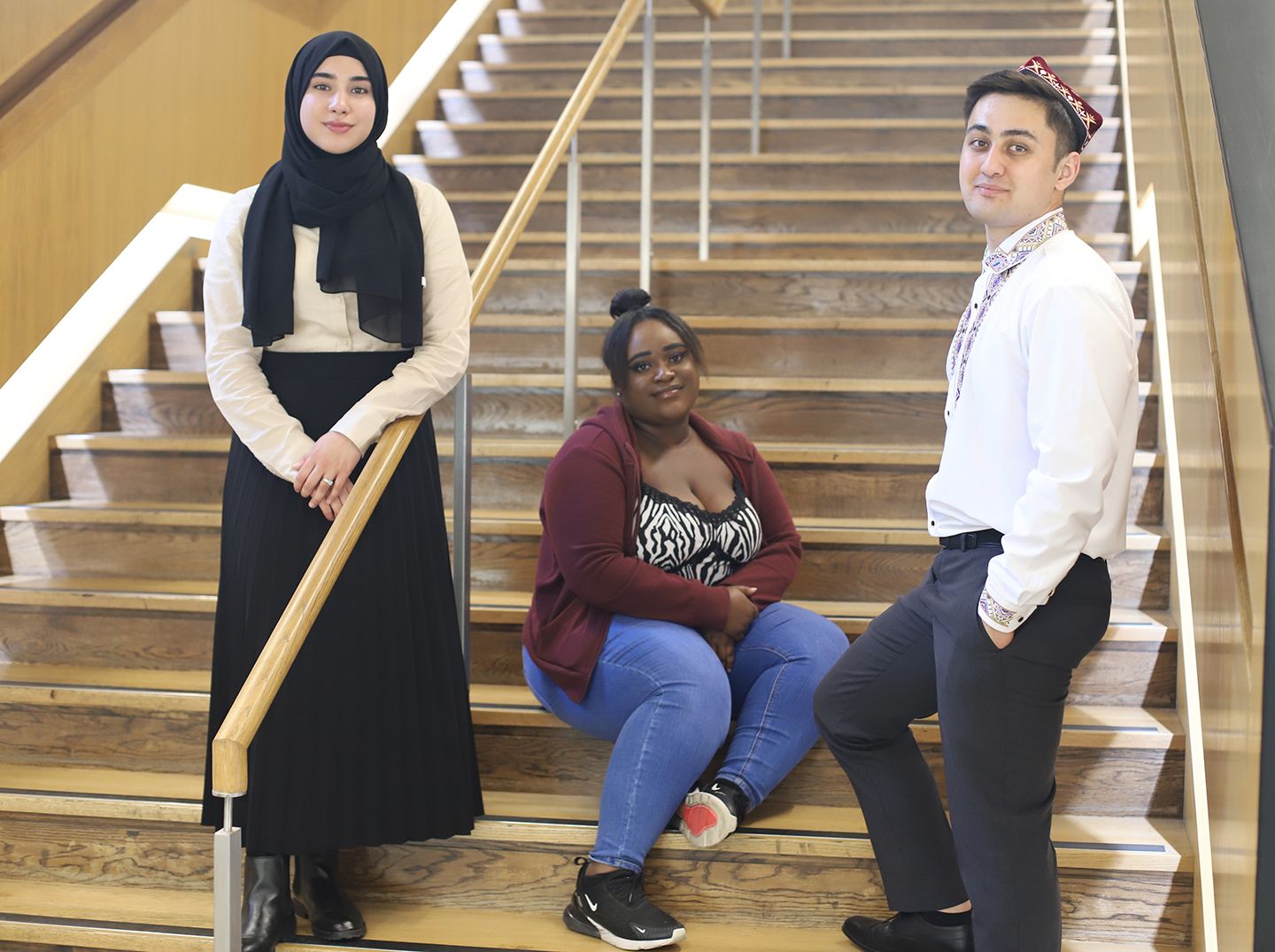 Three young students of varying race and culture, on the stairs in Pavilion.