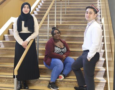 Three young students of varying race and culture, on the stairs in Pavilion.